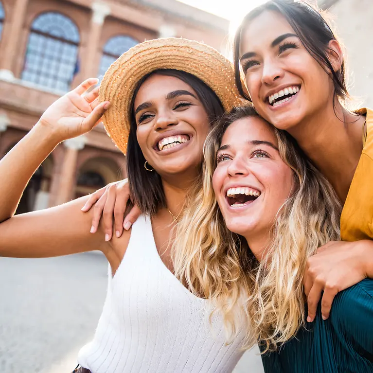 Verschieden Personen sitzen an einem Tisch und lachen. Auf dem Tisch kann man Laptops sehen.