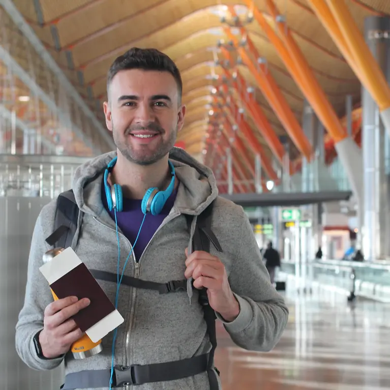 Ein Mann steht mit einem Reisepass in der Hand am Flughafen.