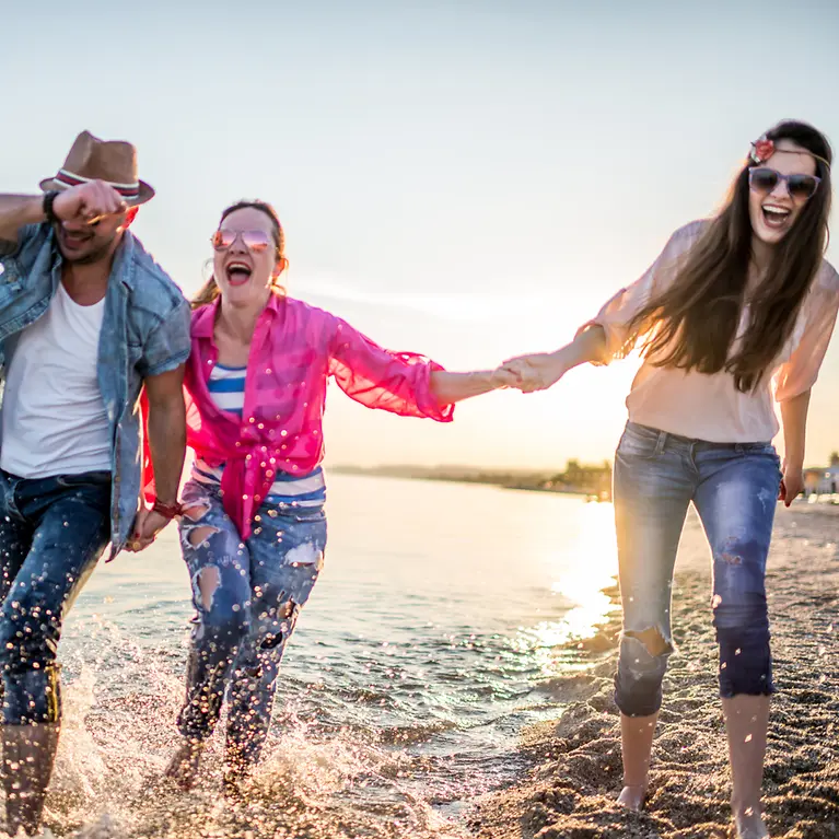 Drei Freunde gehen am Wasser spazieren und tragen alle eine Sonnenbrille.