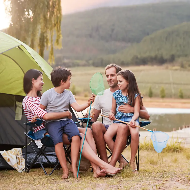 Mutter, Vater und ihre Kinder sitzen vor einem Zelt. Im Hintergrund ist Wasser zu sehen. 