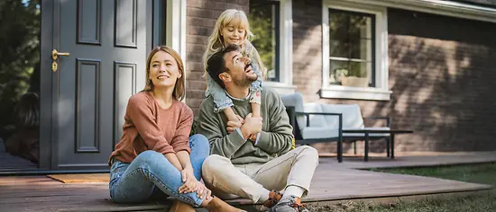 Junge Familie sitzt zufrieden vor ihrem Haus